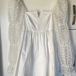 Vit klänning från Labelrail x Collyer Twins - Elegant vit klänning med långa, transparenta ärmar dekorerade med blommigt mönster. Klänningen har en liten v-ringad design. Endast använd på student så i fint skick. Perfekt längd för mig som är 167 cm🌸