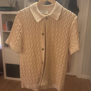 Beige stickad kortärmad kofta från Les Deux - Säljer en stilren beige stickad skjorta från Les Deux. Koftan har korta ärmar och knappar framtill. Perfekt för en avslappnad men ändå elegant look.