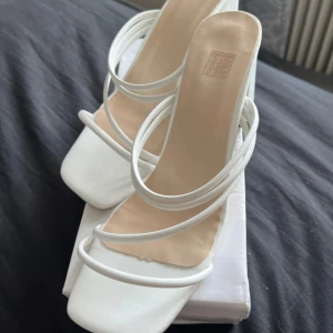 Vita klackskor med remmar - Eleganta vita klackskor med flera tunna remmar och fyrkantig tå. Perfekta för en stilren look. Klacken är bred och stabil, vilket ger extra komfort.