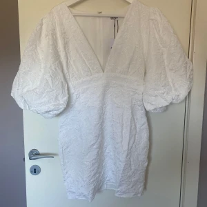 Vit klänning med puffärmar - Säljer en ursnygg studentklänning/vit klänning med djup v-ringning och puffiga ärmar. Alldeles ny, från Showpo med prislapp kvar. Finns i storlek 38/M men även 36/S, normal i storlek.
