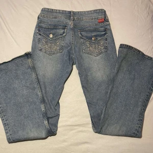 Blå jeans med broderade fickor - Hej, säljer dessa snygga blå jeans med broderade detaljer på bakfickorna! de är bootcut & lowwaist, i nyskick.