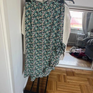 Blommig klänning med volangdetaljer - Säljer en söt blommig klänning med volangdetaljer. Klänningen har en härlig mix av gröna och vita blommor på en svart bakgrund. Perfekt för sommarens alla tillfällen!