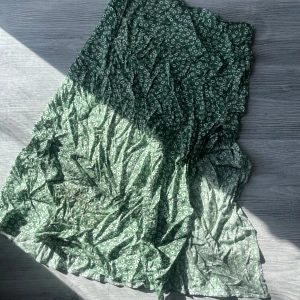 Grön blommig kjol - Säljer en grön kjol med ett sött blommönster. Kjolen har en luftig och bekväm passform, perfekt för varmare dagar. Den är tillverkad i ett lätt material som ger en skön känsla. Har en slits på benet som inte går allt för högt upp, behöver strykas 