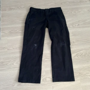 Svarta byxor från Dickies - Säljer ett par svarta byxor från Dickies i modellen Slim Straight. Byxorna har en klassisk design med hällor för bälte och en knappstängning. Perfekta för en stilren look. Baggy.