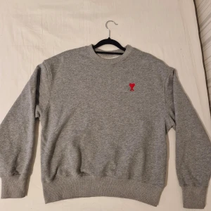 Grå ami sweatshirt - Säljer en stilren grå sweatshirt från Alexandre Mattiussi med ett rött broderat hjärta på bröstet. Tröjan har långa ärmar och ribbade muddar vid ärmslut och nederkant. Perfekt för en avslappnad look. Inga defekter. Tveka inte att höra av dig, priset är inte hugget i sten.👌💯