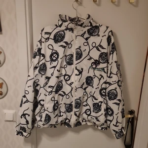 Vit mönstrad jacka från Diesel - Säljer en cool vit jacka från Diesel med ett unikt svart mönster. Jackan har dragkedja och långa ärmar, perfekt för att sticka ut i mängden. Den har även en broderad logga på framsidan. Perfekt för dig som gillar att ha en unik stil!