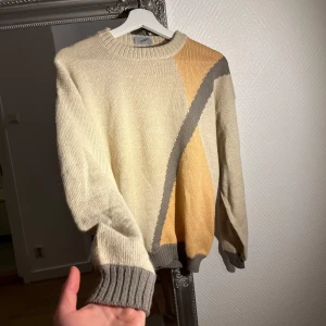 Beige och orange stickad tröja från Luomo - Säljer en unik stickad tröja från Luomo i beige och orange med grå detaljer. Tröjan har ett geometriskt mönster och långa ärmar. Perfekt för att hålla sig varm och stilren under kyligare dagar.