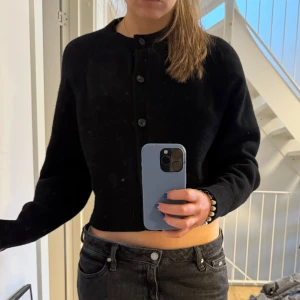 Svart kofta från COS - Säljer en stilren svart kofta från COS i storlek L. Koftan är tillverkad av 100% ull och har en klassisk design med knappar framtill. Perfekt för att hålla sig varm och snygg under kyligare dagar.