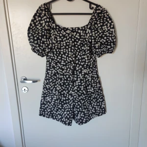 Svart blommig playsuite  - Säljer en söt svart play suite med vita blommor från H&M. Den har korta ärmar och knappar framtill. Perfekt för en somrig look! 🌸