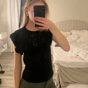 Svart spetsblus - Säljer en elegant svart spetsblus med korta ärmar och volangdetaljer. Perfekt för en stilren look. Passar bra till både jeans och kjol.