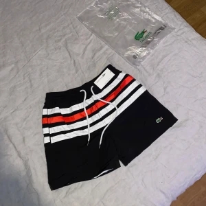 Badshorts från Lacoste  - Hej! Säljer mina Svart Lacoste shorts i storlek S/M. Shortsen är helt oanvända och i ny skick👍. Hör gärna av dig om du har några frågor eller funderingar 😊
