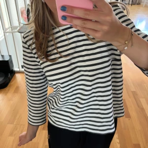 Randig svartvit tröja med dragkedja - Säljer en svartvit randig tröja med trekvartsärm och rund hals. Tröjan har en snygg dragkedja i ryggen som detalj och är i ett mjukt bomullstyg.