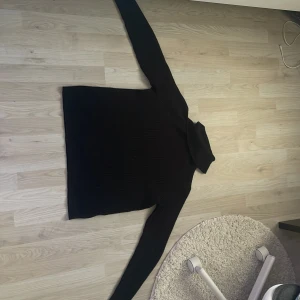 Svart polotröja från Jacqueline de Yong - Svart ribbstickad polotröja från Jacqueline de Yong i storlek XS. Tröjan har lång ärm och hög polokrage, perfekt för lager-på-lager och en clean look. Materialet är mjukt och stretchigt, vilket gör den både bekväm och snygg.