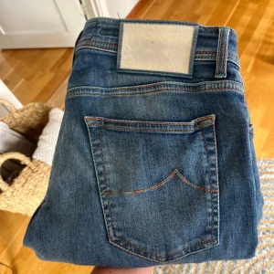  Jacob Cohen jeans - Snygga blå jeans från Jacob Cohen med klassisk femficksdesign, knappar med färgdetaljer och broderad logga på myntfickan. Jeansen har en rak passform och är tillverkade i mjukt bomullsjeansmaterial. Perfekta för dig som gillar stilrena och bekväma jeans.