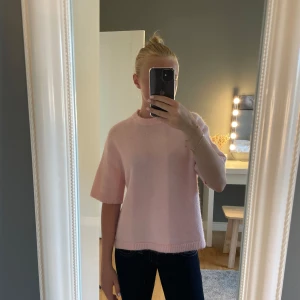 Stickad T-shirt  - Superfin ljusrosa stickad T-shirt med korta ärmar och rund hals. Tröjan har en loose passform och är gjord i mjukt material som känns lyxigt. Perfekt att styla med jeans eller kjol för en chill look.