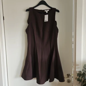 Brun ärmlös kortklänning H&M - Snygg brun ärmlös klänning från H&M med klassisk rund halsringning och lätt utställd kjol. Klänningen har en enkel och stilren design, perfekt för dig som gillar minimalistiskt mode. Dragkedja i ryggen för enkel påklädning.