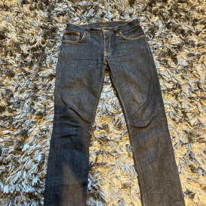 Mörkblå jeans från Nudie Jeans W34 L34 - Snygga mörkblå jeans från Nudie Jeans. Jeansen har kontrastsömmar, fem fickor och är tillverkade i slitstarkt denim. Perfekta för dig som gillar stilrena och tidlösa jeans med bra passform.