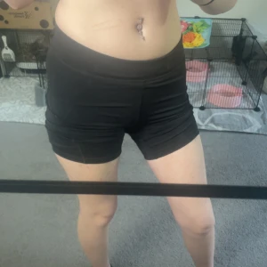 Svarta träningstights shorts OTP - Svarta, tighta träningstights shorts från OTP i storlek 36/38. De är högmidjade och gjorda i ett stretchigt syntetmaterial som sitter skönt på kroppen. Perfekta för gymmet eller löprundan, med en clean och sportig look.