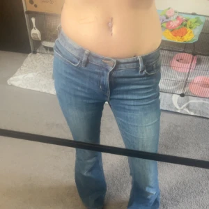 Blå bootcut jeans - Säljer ett par klassiska blå jeans med bootcut passform. Jeansen har låg midja, fem fickor och snygga kontrastsömmar. Tillverkade i slitstarkt denim med en lätt utsvängd benvidd som ger en retro vibe. Perfekta till sneakers eller boots.