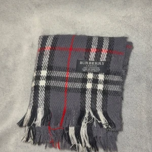 Rutig kashmirhalsduk från Burberry - Snygg halsduk från Burberry i 100% kashmir med klassiskt rutigt mönster i grått, svart, vitt och röda detaljer. Mjukt material och fransar i ändarna. Perfekt accessoar för att lyfta din outfit med en lyxig touch.