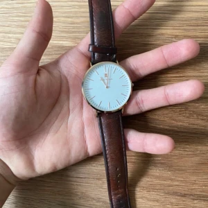 Klassisk klocka från Black Oak - Stilren klocka från Black Oak med vit urtavla, guldigt runt boett och brunt läderarmband. Minimalistisk design med tunna indexmarkeringar och elegant känsla. Perfekt accessoar för dig som gillar klassisk och tidlös stil.