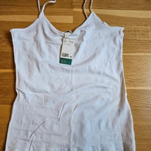 Vitt linnefrån H&M, storlek L - Enkel och stilren vitt linne från H&M i storlek L. Toppen har smala axelband, perfekt för varma dagar. Tillverkad i mjuk bomull som känns skön mot huden. Snygg att matcha med jeans eller kjol för en clean look. Dova fläckar som kommer från butik. 
