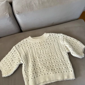 Vit stickad tröja från Zara - Superfin vit stickad tröja från Zara med hålmönster och ribbade muddar. Tröjan har en lite boxig passform och trekvartsärmar, perfekt för lager-på-lager. Mjuk och mysig, passar till jeans eller kjol.