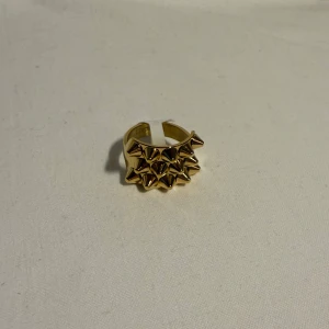 Guldig ring med nitar, storlek 8 - Cool statementring i guld med flera spetsiga nitar framtill. Ringen har en bred design och är perfekt för dig som vill sticka ut med en edgy accessoar. Passar storlek 8 och ger en riktigt tuff vibe till din stil.