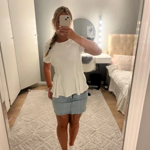 Vit peplumtop från Sense Woman - Supersöt vit peplumtop från Sense Woman med korta ärmar och rund hals. Toppen har figurnära passform upptill och volangliknande peplum nedtill som ger en snygg siluett. Perfekt att styla med jeans eller kjol för en fräsch look.