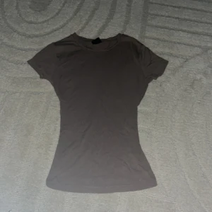 Brun tight t-shirt i bomull - En basic brun t-shirt med tight passform och korta ärmar. Gjord i mjuk bomull, perfekt för en clean och enkel look. Rund halsringning och utan tryck eller mönster, passar till allt.