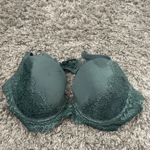 Grön spets-bh med vadderade kupor - Snygg grön bh med vadderade kupor och fina spetsdetaljer längs kanterna. Justerbara axelband och hakknäppning bak. Perfekt för dig som gillar en feminin look med extra stöd och stil.