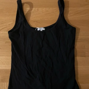 Svart linne från Bubbleroom - Enkel svart linne från Bubbleroom med klassisk rund halsringning och breda axelband. Tillverkad i mjuk bomull som känns skön mot huden. Perfekt att styla lager på lager eller bara som den är till jeans eller kjol.