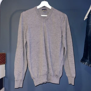Grå stickad tröja från Lyle & Scott - Grå stickad tröja från Lyle & Scott med v-ringning och broderad logga på ärmen. Klassisk modell med ribbade muddar och lång ärm, perfekt för lager-på-lager. Enkel att matcha med jeans eller chinos. Tröjan är i storlek s, är 100% ull samt aldrig andvänd.                                                    Priset är ej hugget i sten