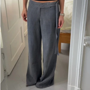 Grå lågmidjade linnebyxor design by si - Snygga grå linnebyxor med låg midja och vida ben från design by si. Byxorna har ett stilrent knytband i midjan och dragkedja i sidan för en clean look. Tyvärr är en del på dragkedjan trasig som på bilderna, men funkar fof att använda och går lätt att fixa. Ordinarie pris var 650kr, slutsålda på hemsidan.