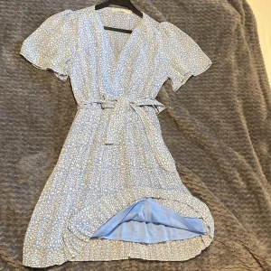 Blå omlottklänning från Retro & Icone - Supersöt blå omlottklänning med vitt leopardmönster från Retro & Icone. Klänningen har v-ringning, är ej genomskinlig, har knytband i midjan och plisserad kjol. Använd två gånger!  