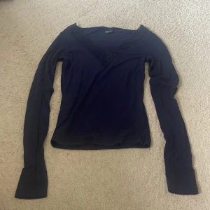 Mörkblå långärmad topp med spets - Snygg mörkblå långärmad topp från Gina Tricot med v-ringning och dekorativ spetsdetalj längs halsringningen. Perfekt att styla med jeans eller kjol för en trendig look. Mjuk och stretchig känsla.