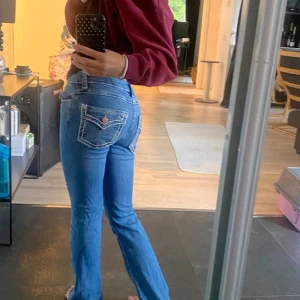 Blå jeans med knappfickor  - Säljer ett par blå jeans med snygga kontrastsömmar och fickor med lock bak. Jeansen har hög midja och raka ben, vilket ger en klassisk och clean look. Perfekta för dig som gillar en tidlös stil med lite edge.