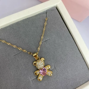 Guldigt halsband med nalle och hjärta - Supergulligt halsband i guldton med en nalleberlock täckt av glittrande stenar och ett rosa hjärta på magen. Kedjan är tunn och tvinnad, perfekt för att ge lite extra bling till din look. Nallen är detaljerad och gnistrar snyggt i ljuset. Ej använd utan kommer från min small business. 