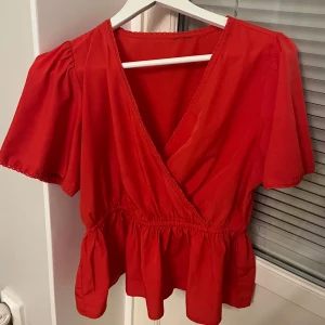 Röd omlottblus med volang veromoda -  röd blus med omlott och v-ringning. Toppen har korta puffärmar och volang nedtill som ger en söt och trendig look. Perfekt att styla med jeans eller kjol för en färgstark outfit. Lapp avklippt.