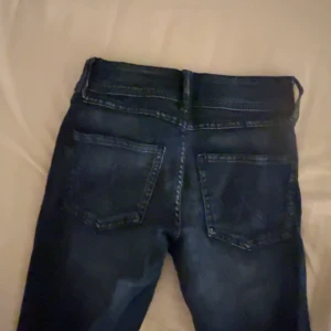 Mörkblå jeans från Gina Tricot - Snygga mörkblå jeans från Gina Tricot med klassisk femficksdesign och dubbla silverknappar i midjan. Jeansen har en bootcut design och är tillverkade i stretchig denim för en bekväm passform. Perfekta till sneakers eller boots. Endast använda 1 gång