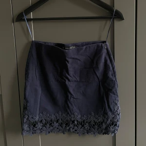 Mörkblå kjol med spetsdetaljer från Zara - Mörkblå kort kjol med spetsdetaljer längs nederkanten. Kjolen har en dragkedja på sidan för enkel på- och avtagning. Från Zara i storlek XS.