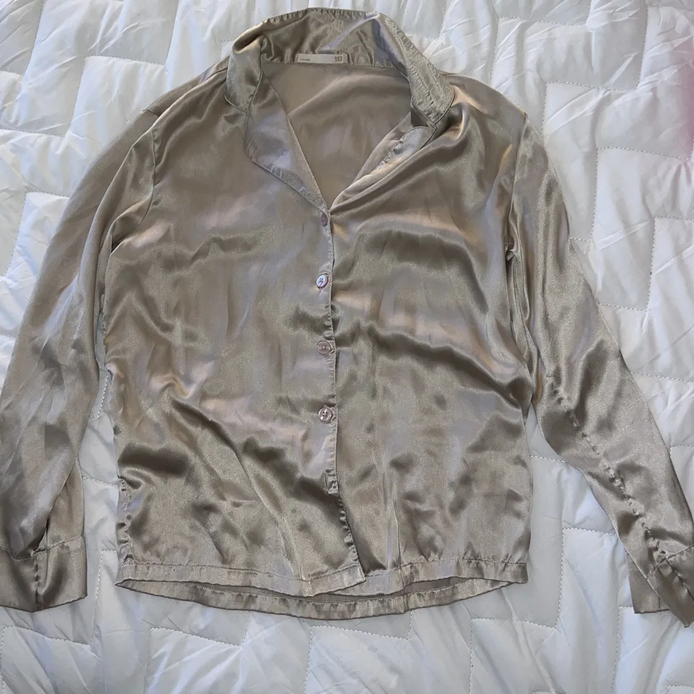 Elegant beige blus i siden med knappar framtill. Perfekt för en stilren look. Blusen har långa ärmar och en klassisk krage.. Muu.