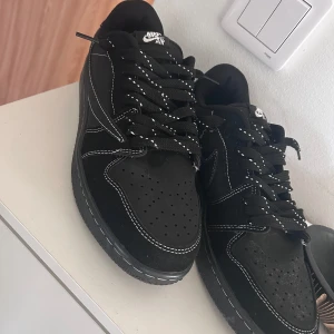 Svarta Nike Air sneakers med vit söm - Snygga svarta Nike Air sneakers med kontrasterande vita sömmar och detaljer. Skorna har en klassisk design med snörning och en unik broderad detalj på hälen. Perfekta för en stilren look.