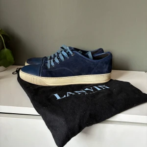 Blå sneakers från Lanvin - Snygga blå sneakers från Lanvin med ovandel i mocka och snörning. Skorna har en vit sula och en stilren design som passar perfekt för en avslappnad look. Perfekta för dig som vill ha både stil och komfort. 8/10 i skick. Ny pris≈5000kr men säljer för bara 1600kr