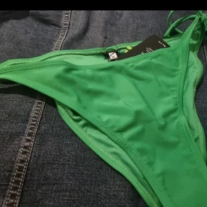 Grön bikiniunderdel - Snygg grön bikiniunderdel med knytband på sidorna. Perfekt för en dag på stranden eller vid poolen. Tillverkad i ett mjukt och bekvämt material.