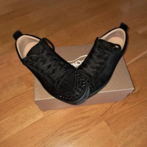 Christian Louboutin svart - Snygga svarta sneakers med nitar på tån och klassisk röd sula. Skorna har snörning och är tillverkade i mocka. Perfekta för att ge en grisch touch till din outfit. 2 tappade nitar men märks inte går också att köpa nya. Pris går såklart att diskutera