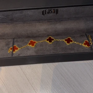 Guldarmband med röda detaljer från Kejsar - Elegant guldarmband från Kejsar med röda fyrklöverformade detaljer. Perfekt för att ge en färgklick till din outfit. Armbandet kommer i en stilren svart förpackning. Helt nytt den är i 16cm riktigt fint smycke.Köpt för  999kr 