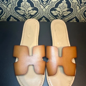 Bruna sandaler från Madden Girl - Snygga bruna sandaler från Madden Girl med en stilren design. De har en bred rem över foten i syntetmaterial och en platt sula för bekväm användning. Perfekta för varma sommardagar.