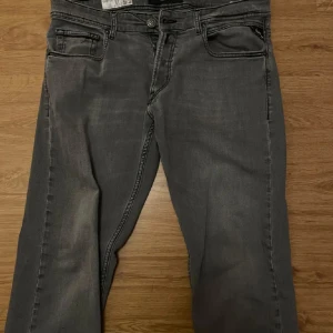 Grå jeans från Replay - Snygga grå jeans från Replay med klassisk femficksdesign och knappgylf. Perfekta för en stilren look. Märkeslappen syns tydligt baktill. Köpte dom för 1800 kr o säljer dom 500 kr, kontakta mig om du har frågor eller funderingar! 