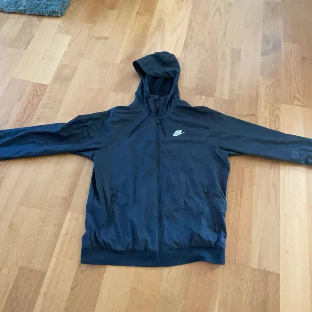 Säljer en stilren svart vindjacka från Nike med dragkedja och huva. Jackan har en klassisk design med Nike-logga på bröstet och är perfekt för blåsiga dagar. Den är långärmad och har en bekväm passform. Passar perfekt nu inför golf starten.. Takit.